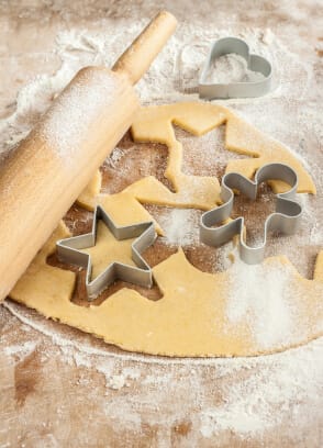 a floured board with cookie dough rolled out featuring a rolling pin and holiday themed cookie cutters