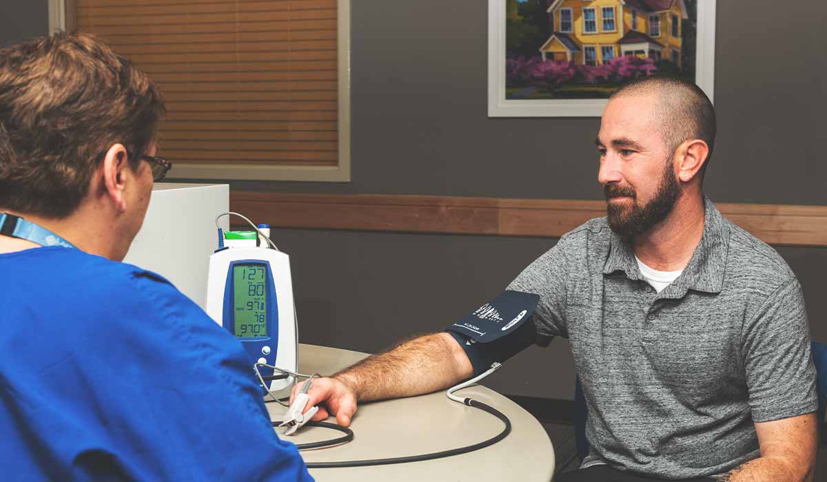 bearded man having blood pressure taken asking questions about addiction treatment