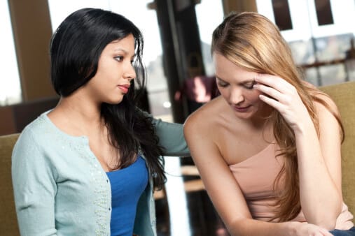 young woman consoling another young woman as they discuss alcohol abuse