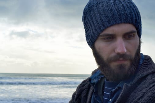 young man with beard in stocking cap on a winter beach reflecting on the facts of alcohol use