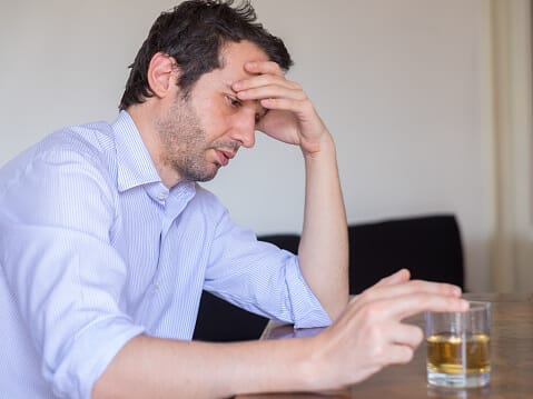 unshaven man with alcoholic drink in front of him and worried look reflecting on alcoholism