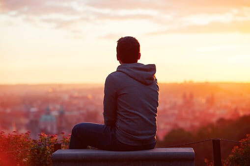 rear view of young patient in hoodie seated on bench overlooking city at sunrise considering how to prepare for alcohol addiction therapy