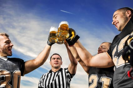 three football players and a referee raising large glasses of beer in a toast
