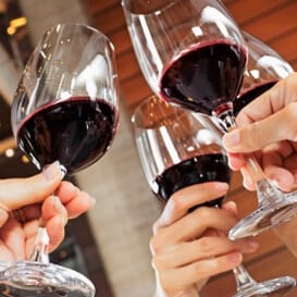 closeup of four hands with full glasses of red wine making a toast