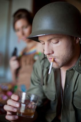 military man with cigarette and alcoholic drink with lady holding gun in background