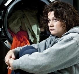 a distraught woman in front of a dryer with clothing spilling out demonstrating the dangers of domestic abuse