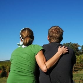 rear view of a man and woman as she places her arm around his shoulder supportively and they look out at a natural landscape