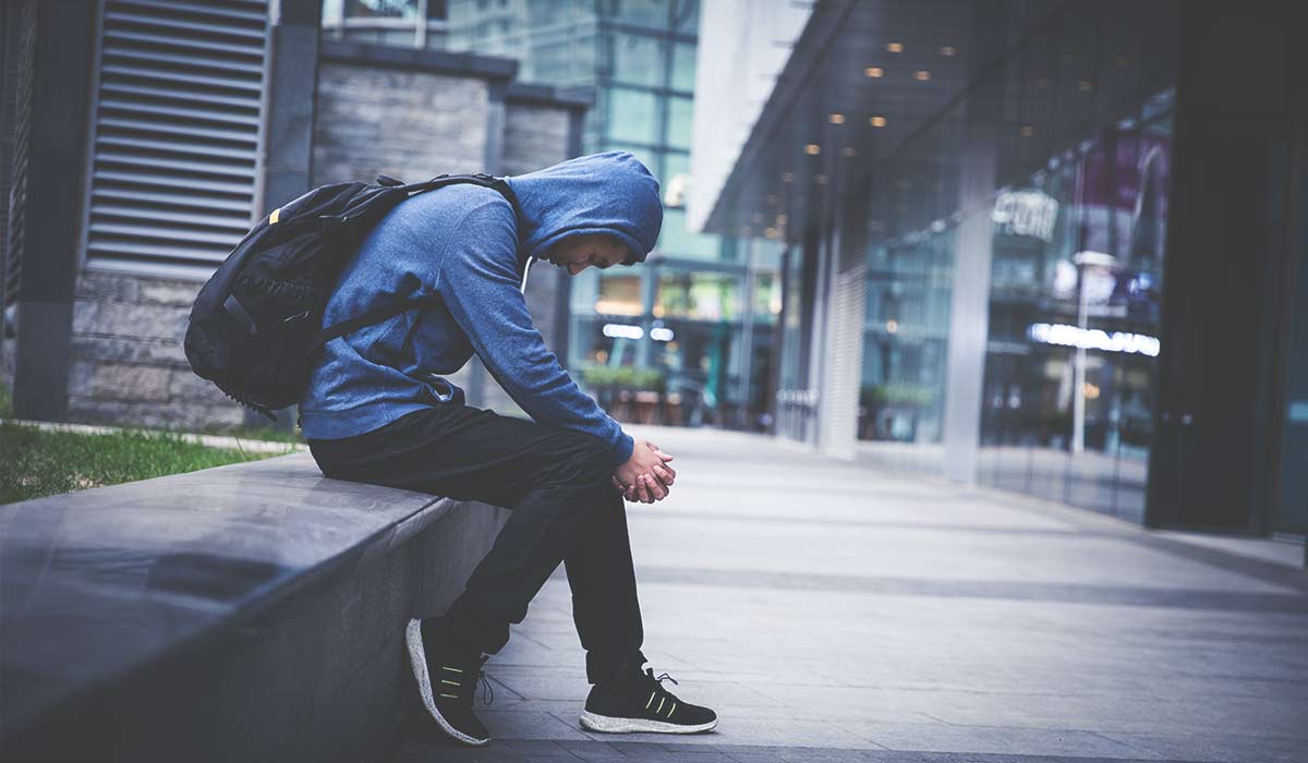 young man in hoodie sitting on ledge demonstrating signs of drug abuse