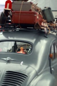 an antique car with suitcases tied to a luggage rack on the top and a child's doll peeking out of the back window