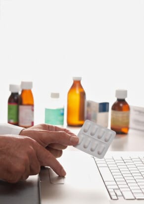 closeup of hands holding prescription drugs and typing on a computer