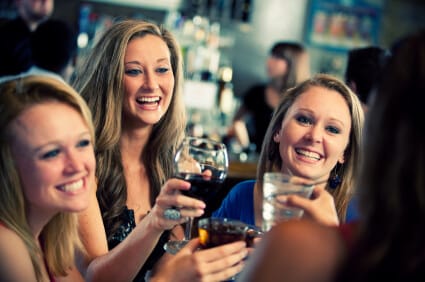 a group of young women at a bar smiling and raising their glasses in a toast