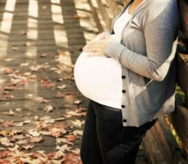 a partial image of a pregnant woman with her hands on her stomach standing on a bridge in autumn illustrating the dangers of being pregnant and addicted to opiates and importance of neonatal abstinence
