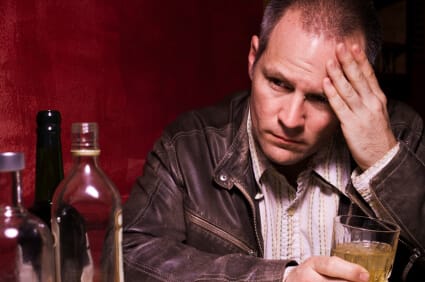 worried man at table with a glass of liquor in his hand and multiple bottle in front of him