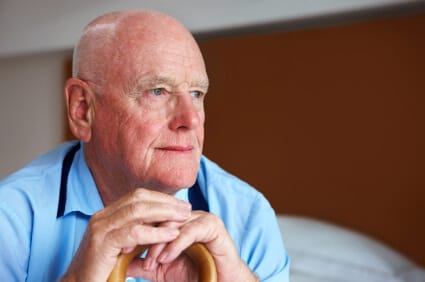 elderly man sitting on bed leaning on cane and looking into the distance